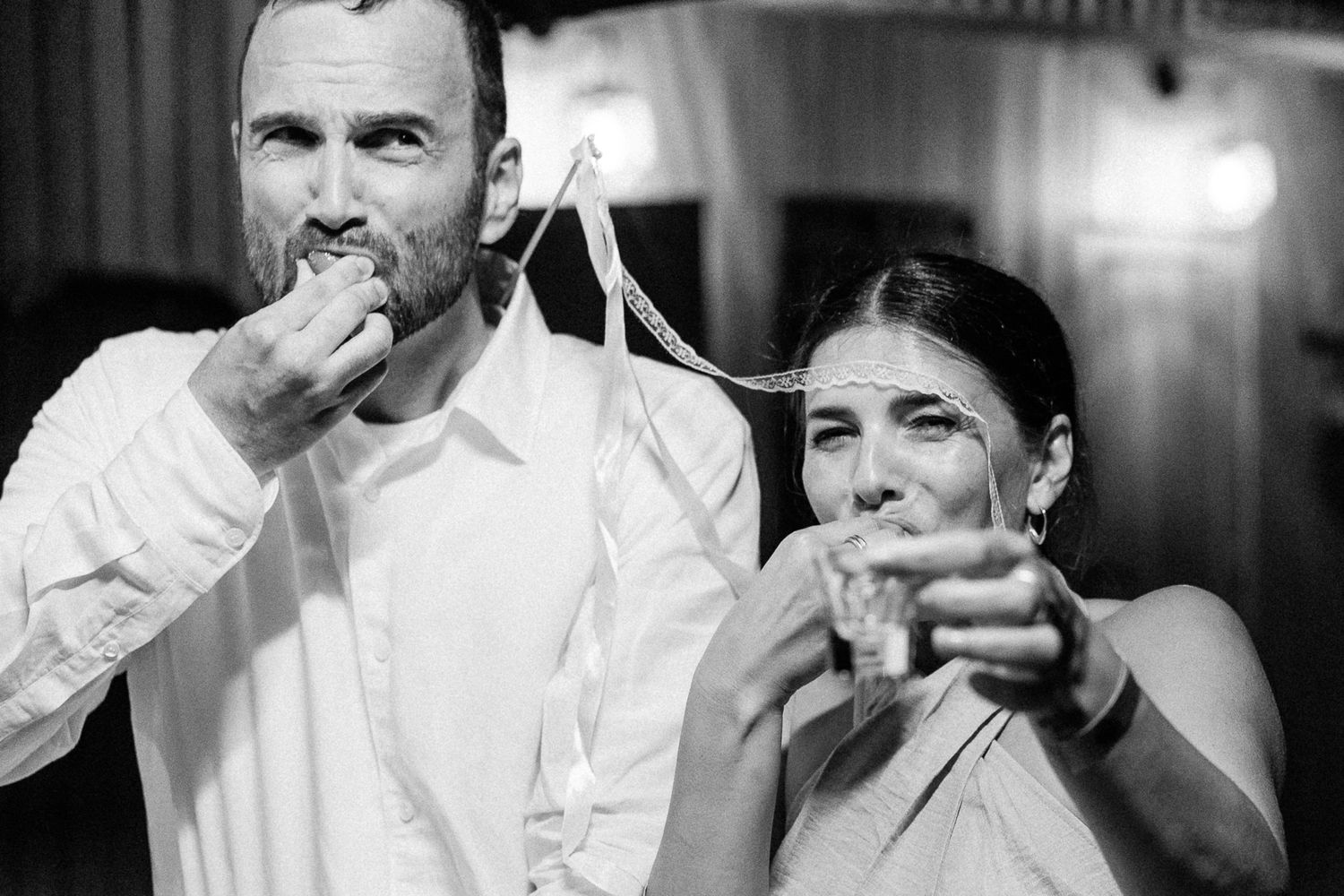 Black and white photo of a man and woman at a wedding reception, blowing whistles and celebrating.