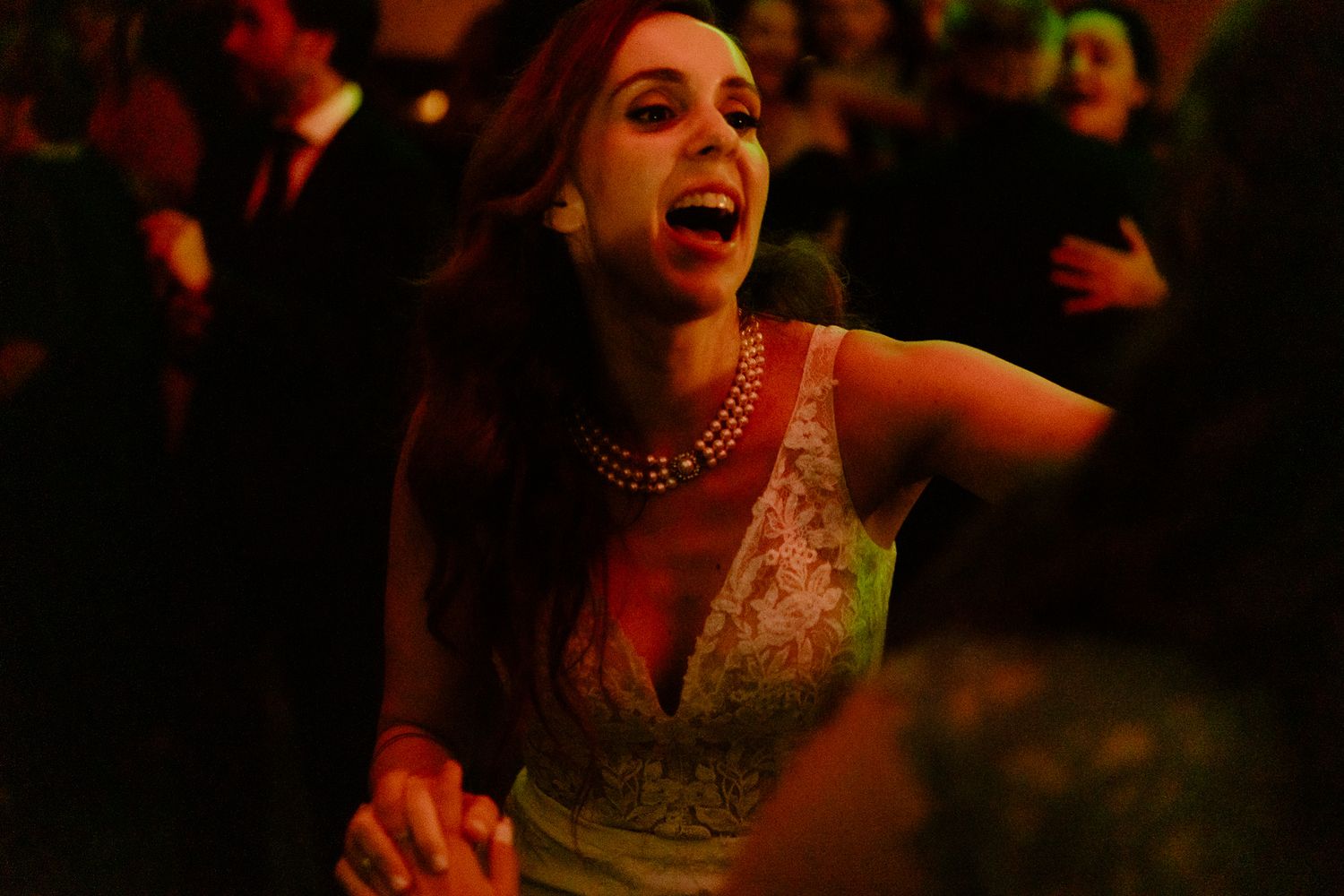 Woman in a lace gown laughing and dancing at a lively wedding reception.