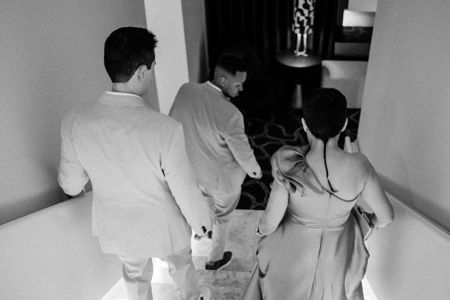 Black and white photo of three people walking down a hallway, dressed in formal attire for a wedding.