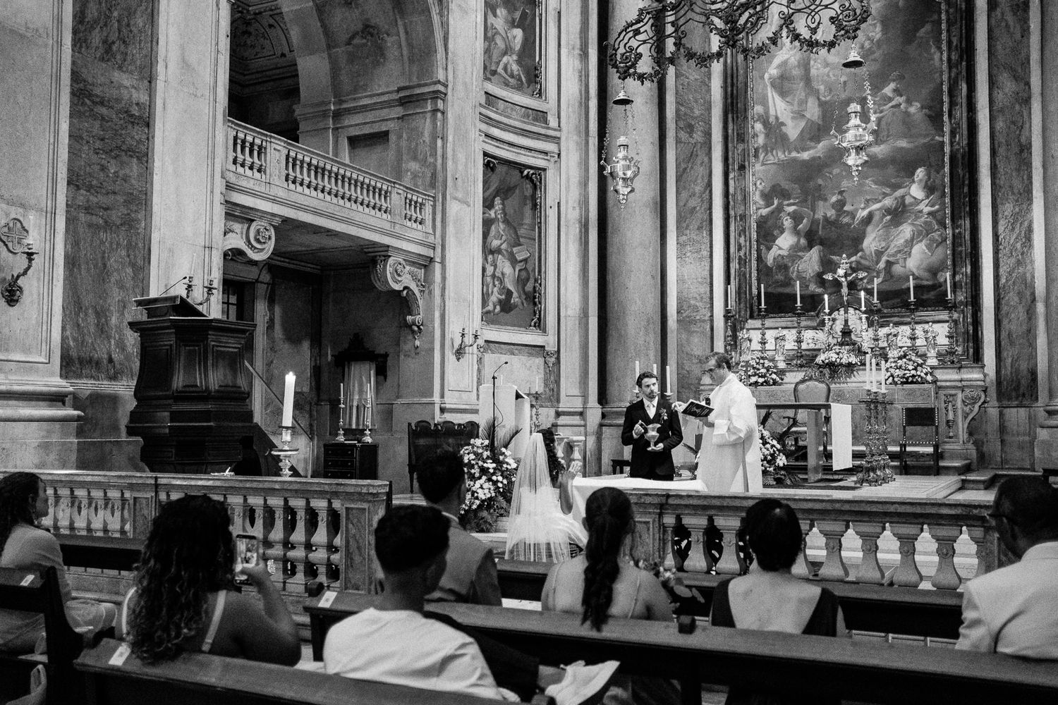 Black and white photo of a wedding ceremony at a church altar with guests seated in pews.