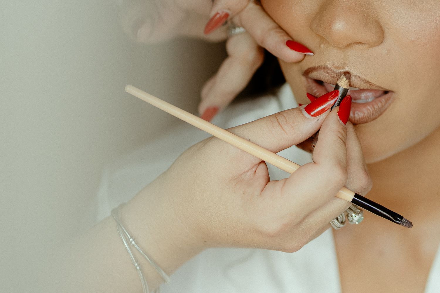 Makeup artist applying lip liner to a woman's lips with a wooden brush tool.