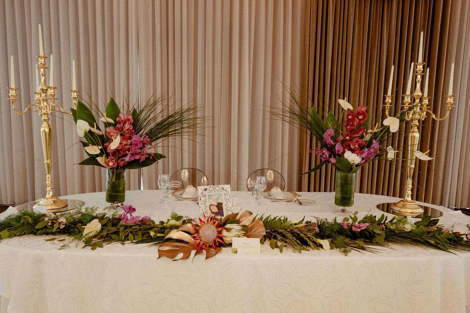 Elegant banquet hall decorated with white drapes, lush floral arrangements, and golden accents for an upscale wedding reception.