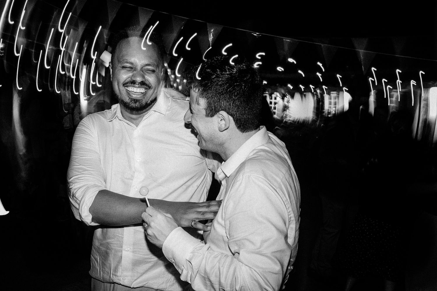 Two men laughing and sharing a joyful moment together at a nighttime event in black and white photo.