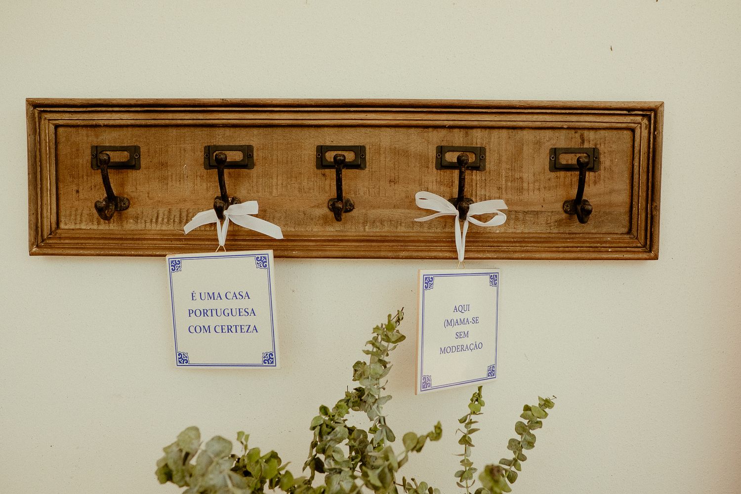 Rustic wooden wall hook rack with decorative cards and eucalyptus plant on white wall.