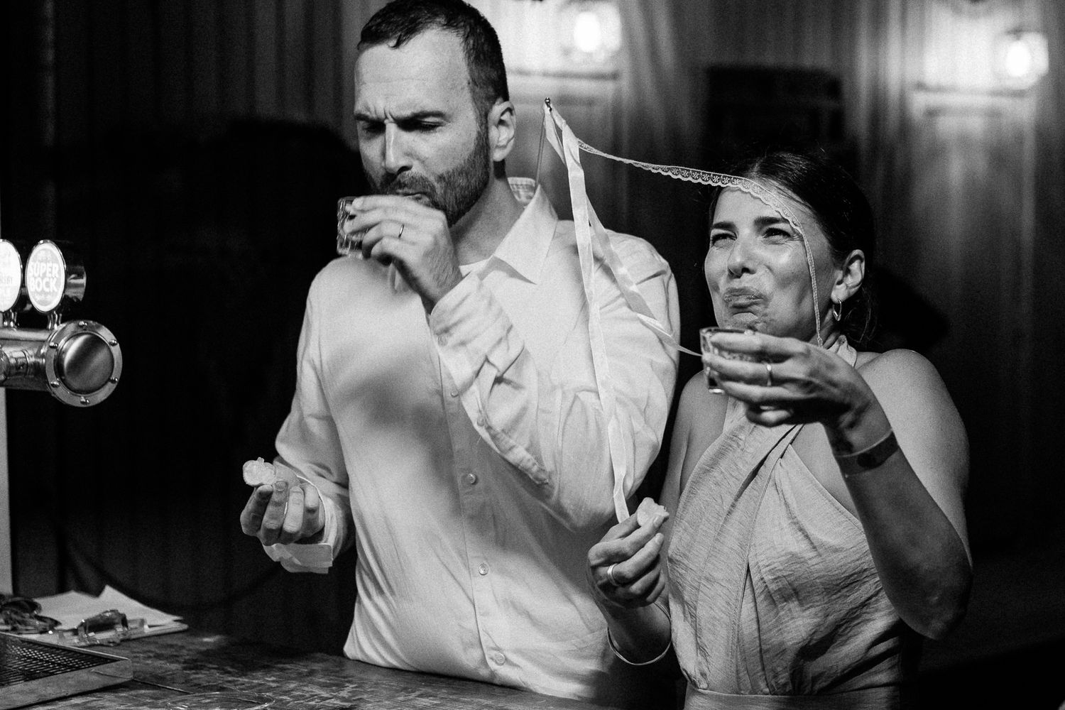 Black and white photo of a man and woman sharing drinks tied together with a string at a party.