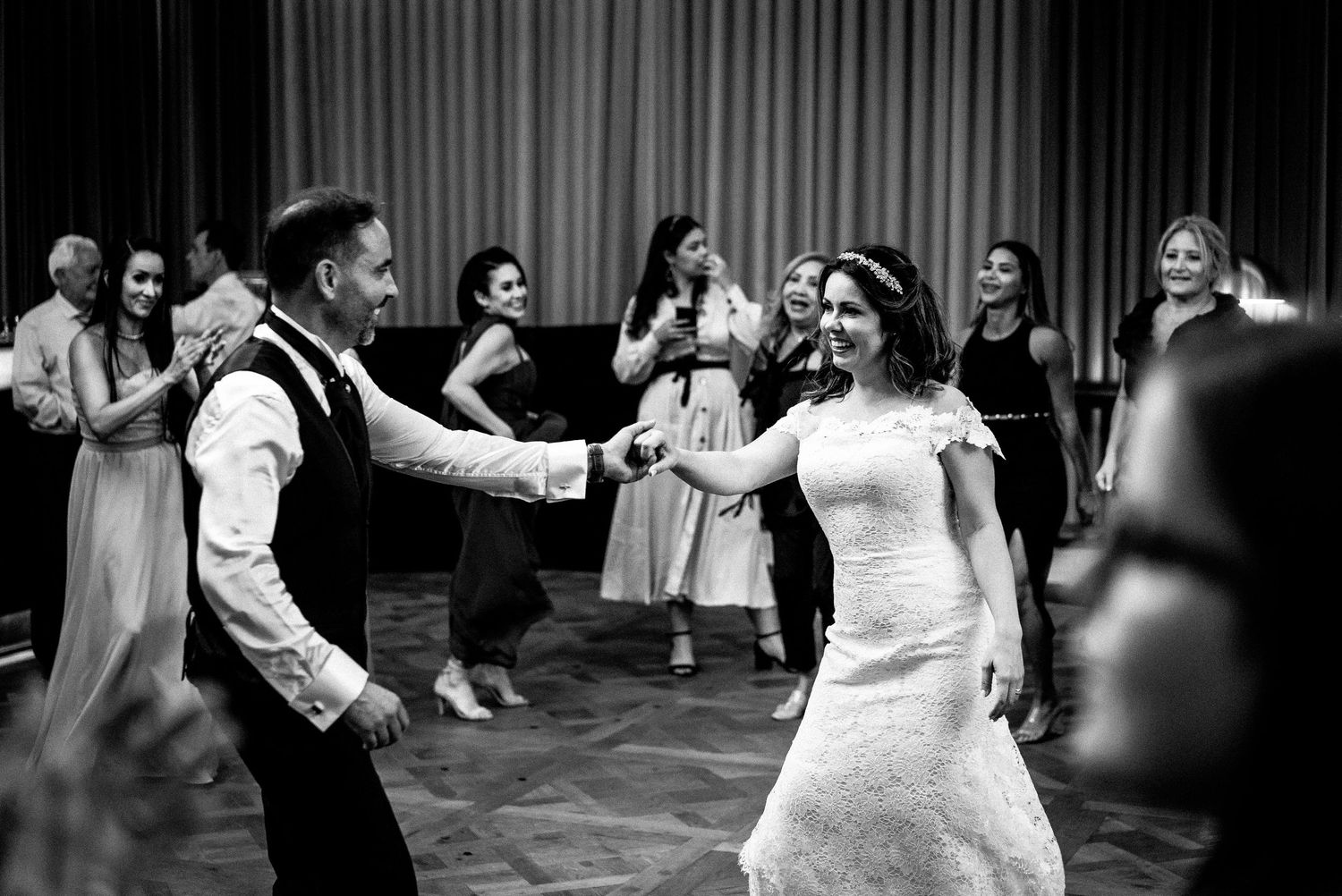 Wedding reception guests dance and celebrate during what appears to be a traditional circle dance or group dance number.