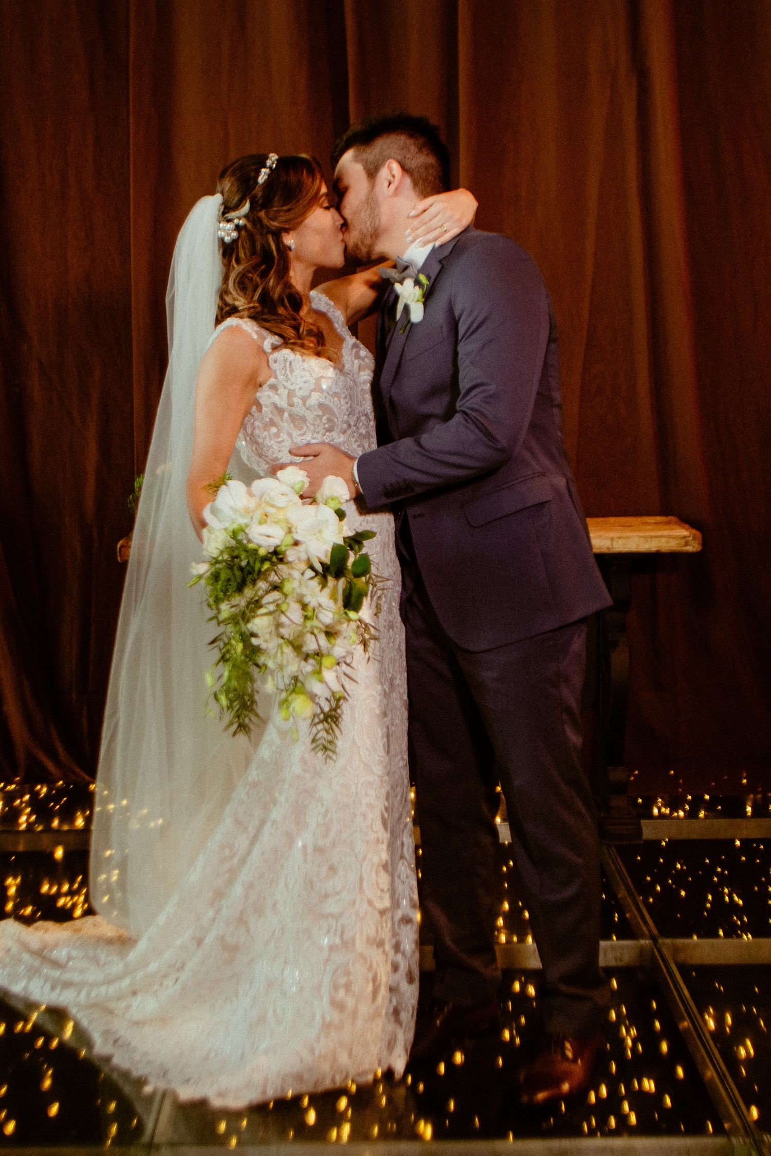 Newlywed couple sharing their first kiss during a romantic wedding ceremony with twinkling lights in the background.