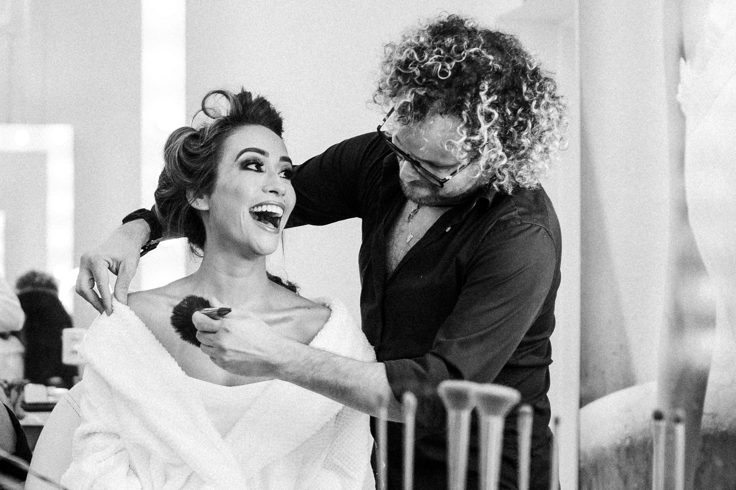 Black and white candid moment of two people sharing laughter during a wedding celebration.