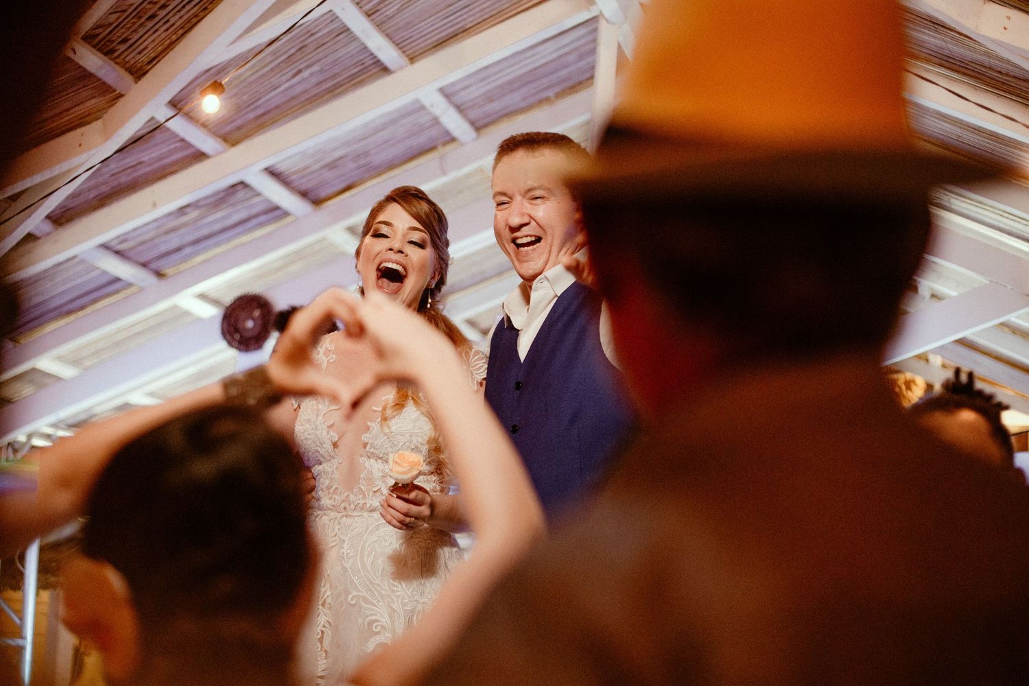 Joyful couple dances with guests during lively wedding reception under warm lighting, captured with motion blur.