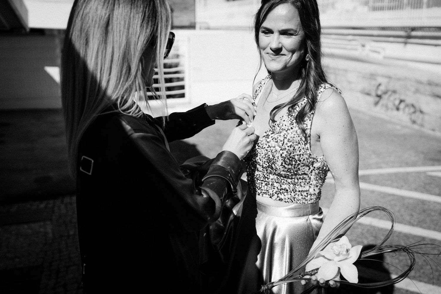 A black and white candid moment shows two people interacting outdoors, one wearing a sleeveless formal dress.