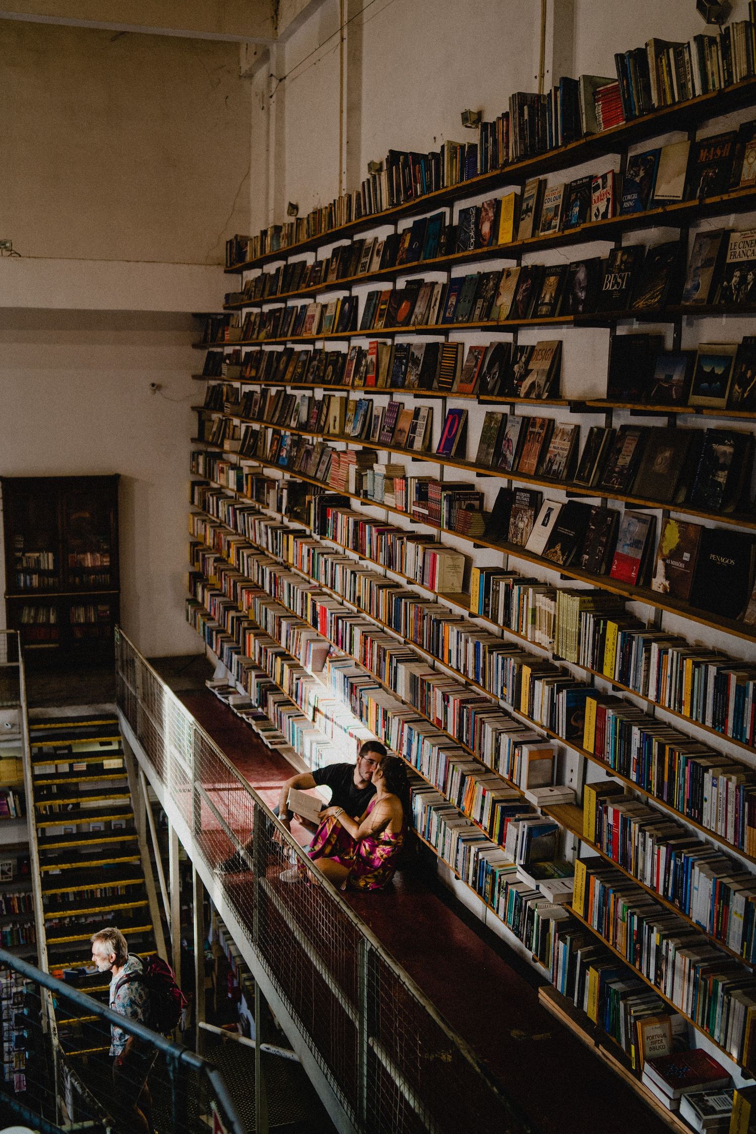 Two people browse extensive bookshelves in a dimly lit multi-level library.