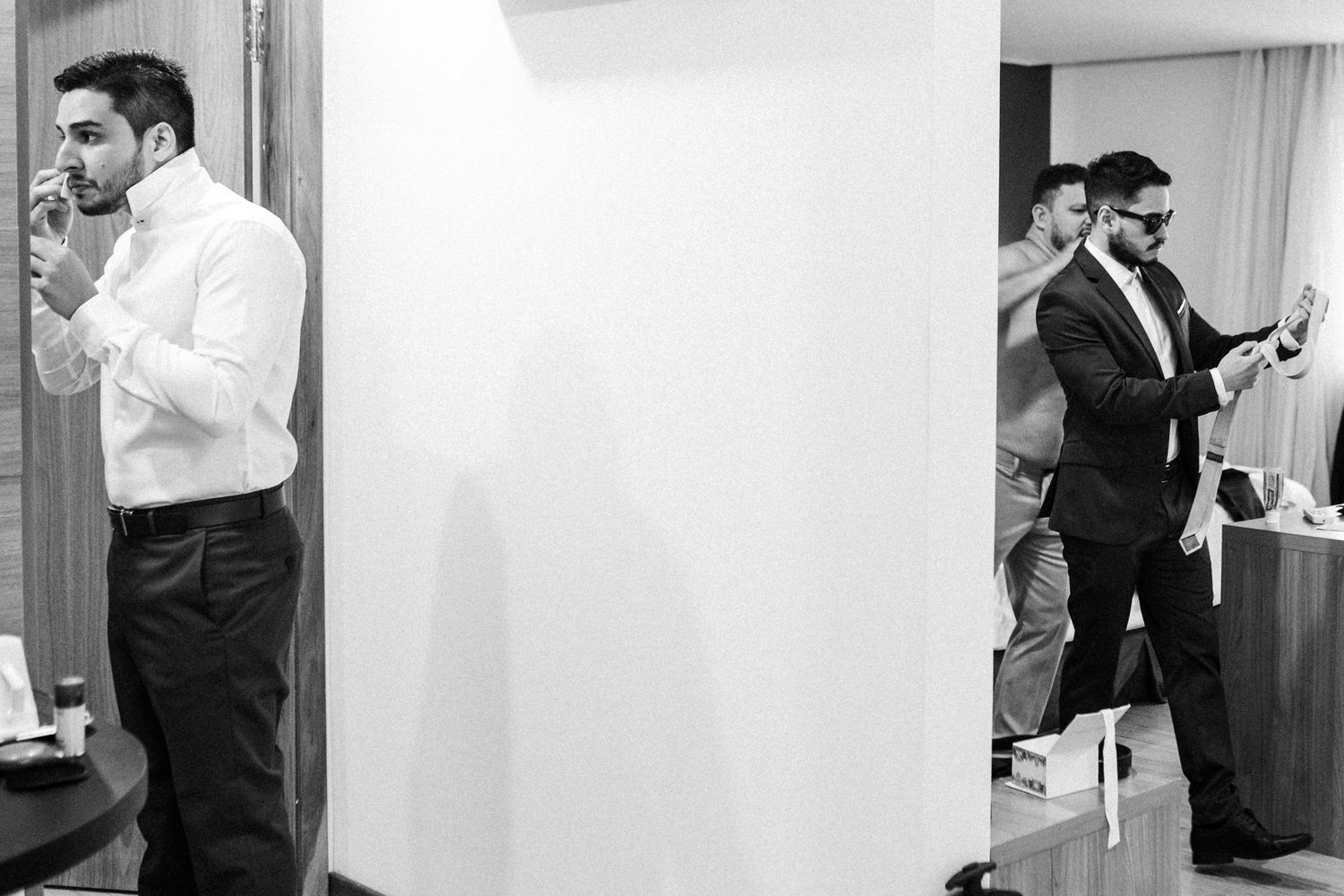 Black and white image showing men in formal attire getting ready in a mirrored room.