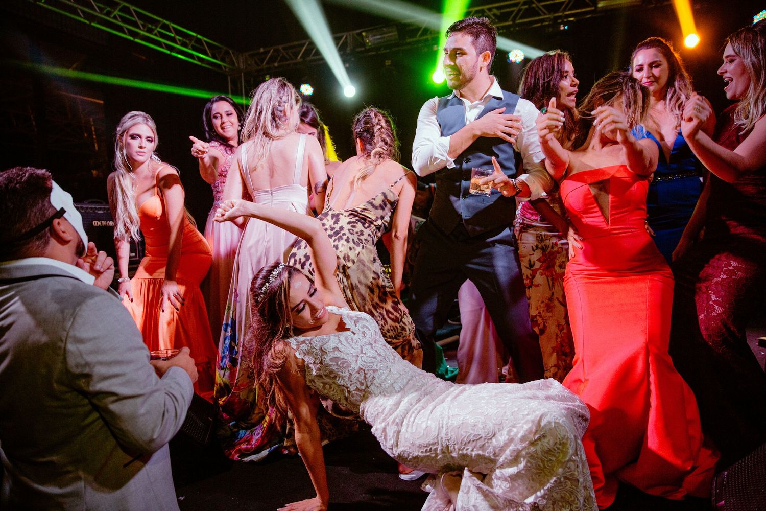 A lively wedding reception scene with dancers under colorful spotlights on a crowded dance floor.
