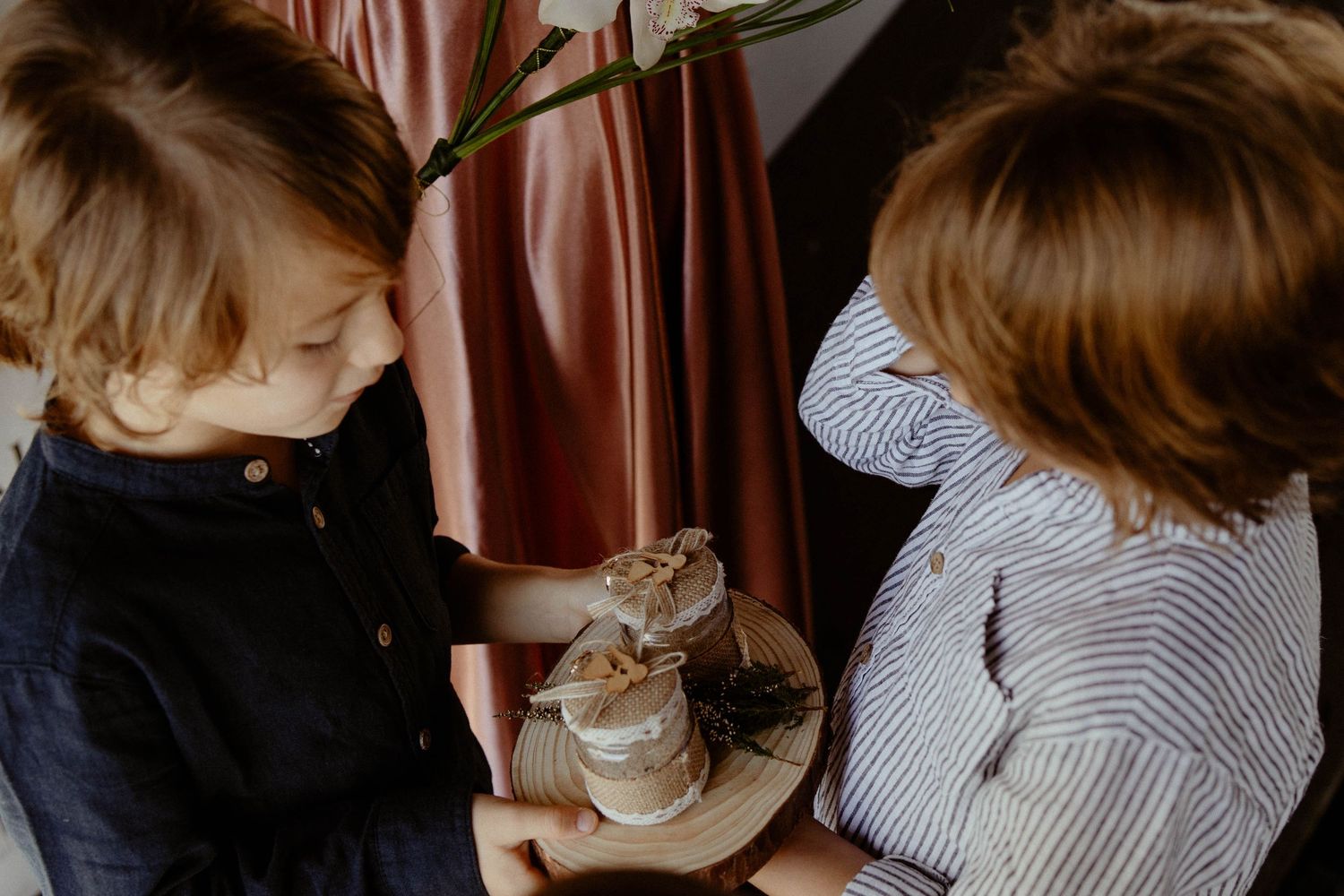 Two children in casual attire sit together while petting a tabby cat resting on a plate.