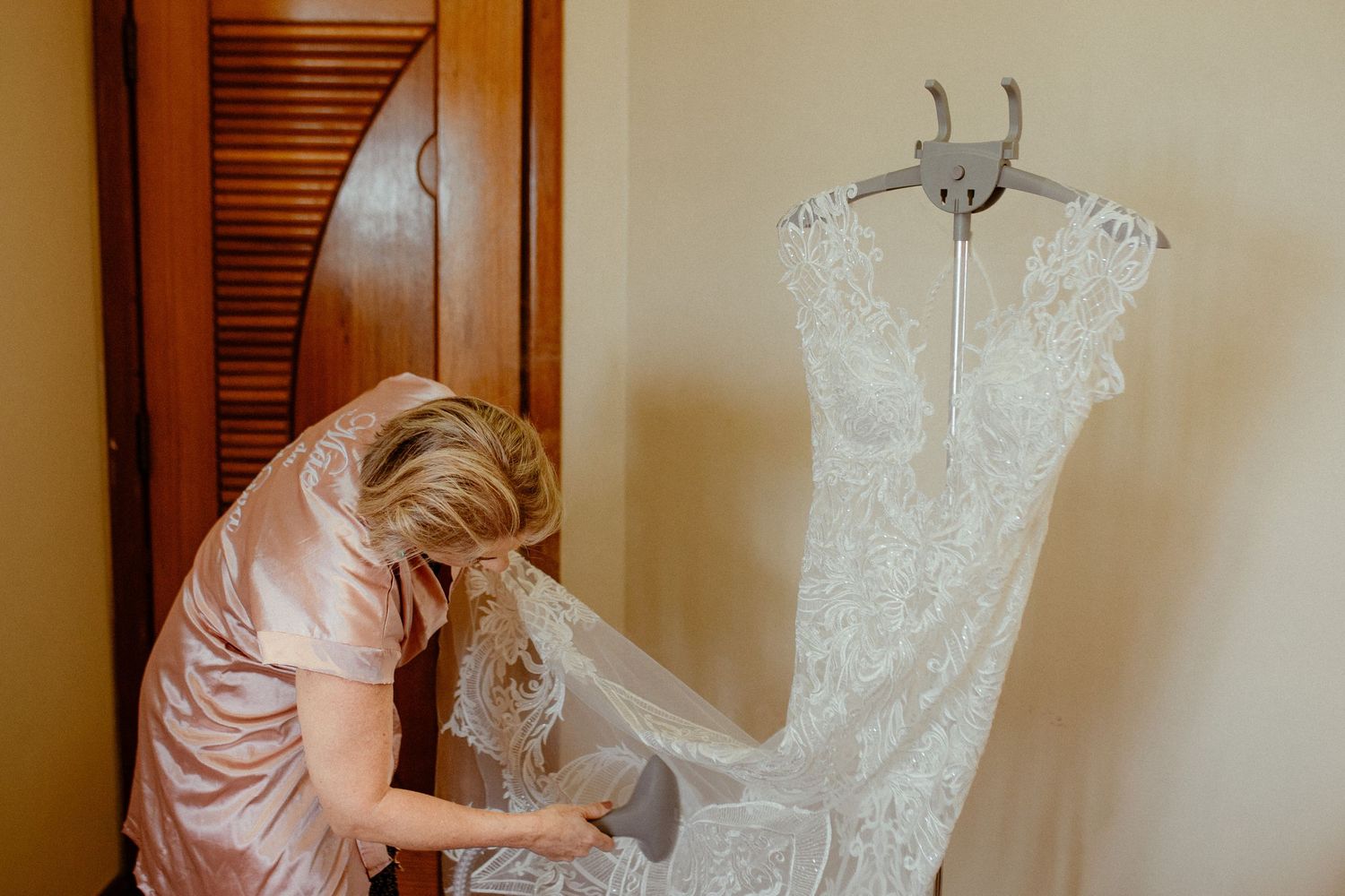 A person in a pink shirt draws alterations on a white wedding dress laid out on a workbench.