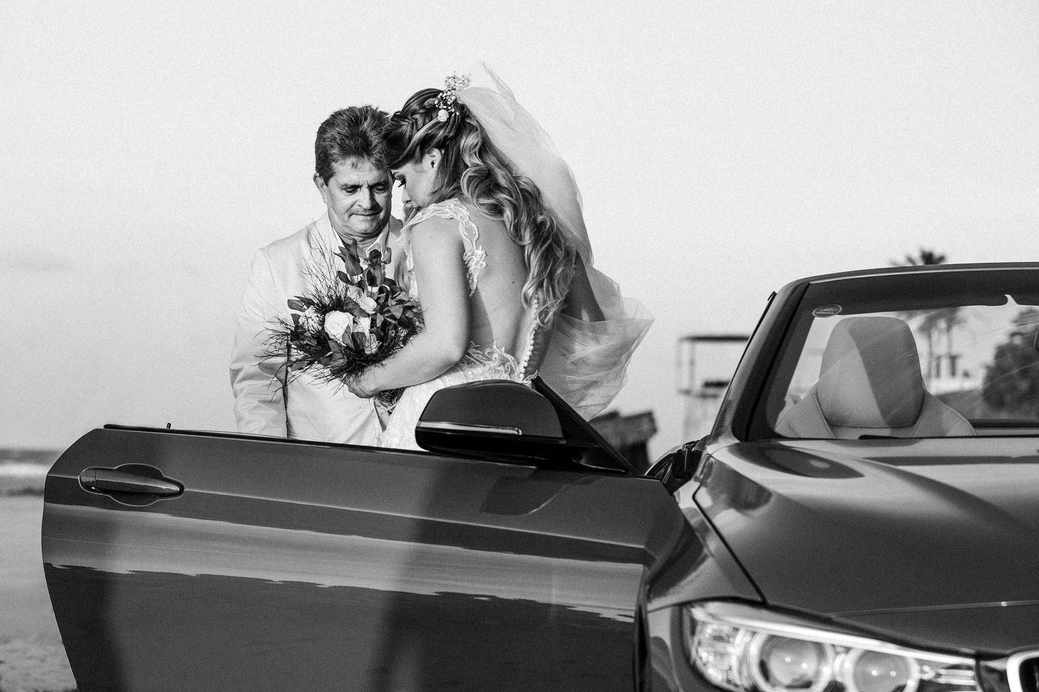 A wedding couple poses romantically on vintage cars in a dramatic black and white photo series.