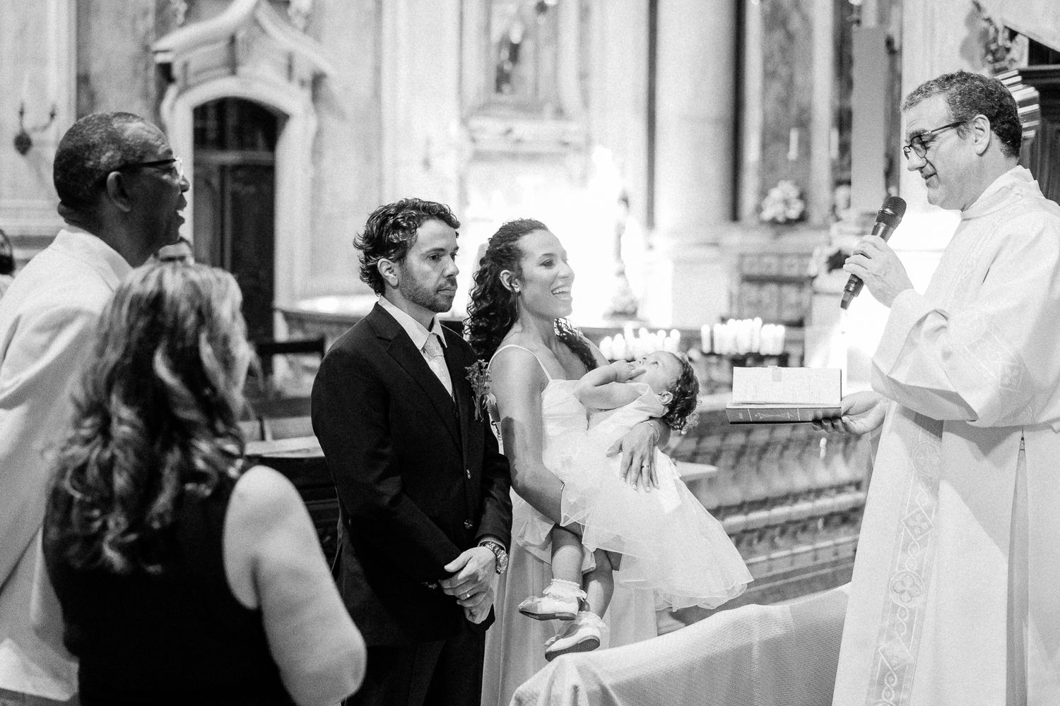 Bride and groom exchange vows before a priest during an elegant church wedding ceremony in black and white.