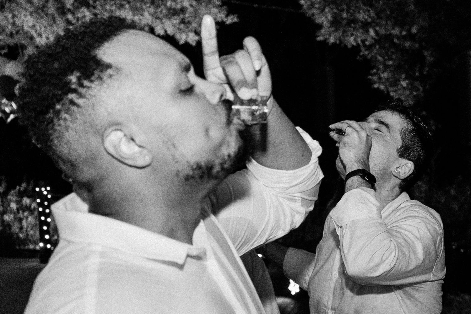 Two men in white shirts taking shots at a party in black and white photo.