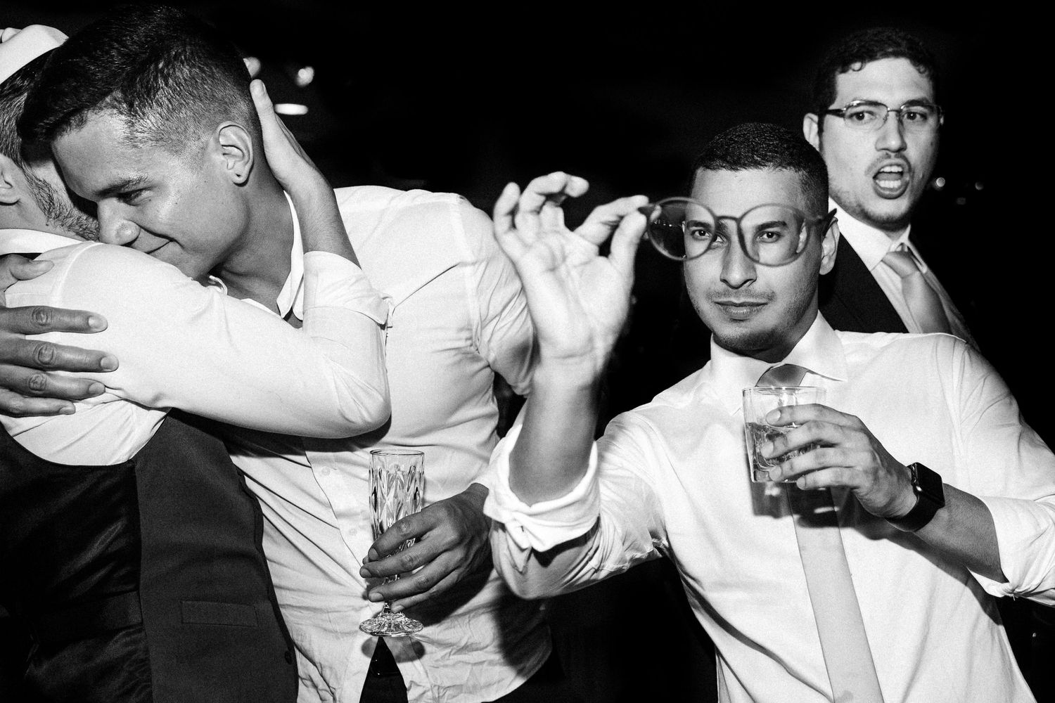 A black and white candid shot of party guests dancing and celebrating with drinks in hand.