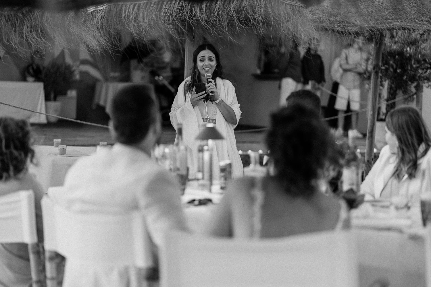 Woman speaking at a microphone during an outdoor wedding reception dinner in black and white photography.