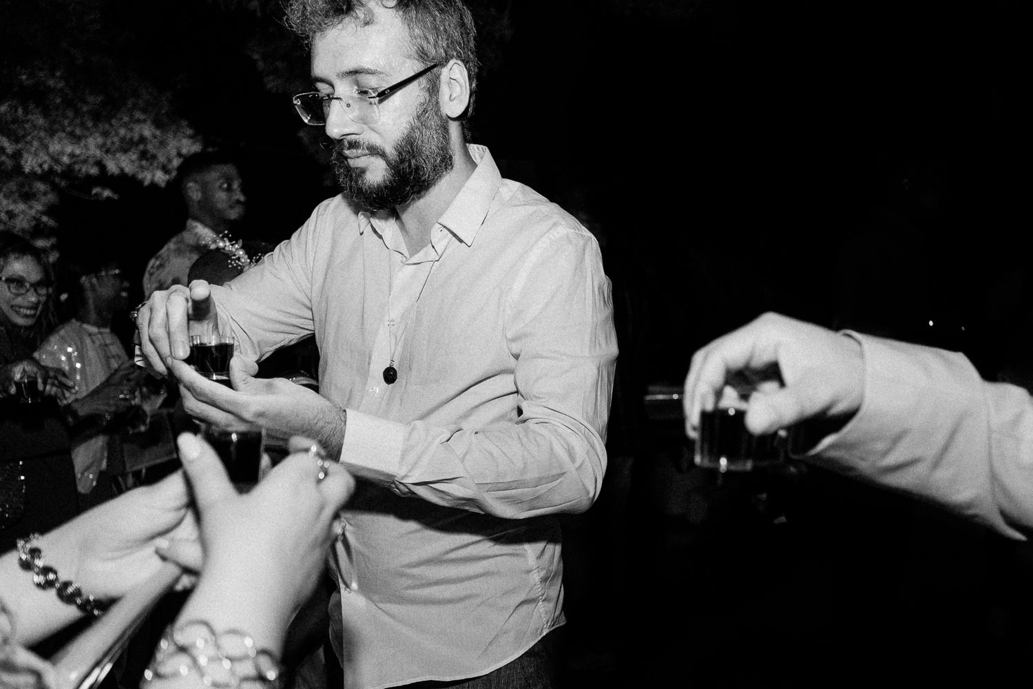 Black and white photo of a bearded man with glasses signing autographs for fans at an outdoor event.