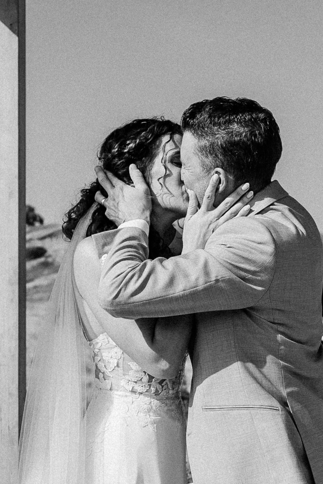 Black and white photo of a bride and groom sharing a romantic first kiss on their wedding day.