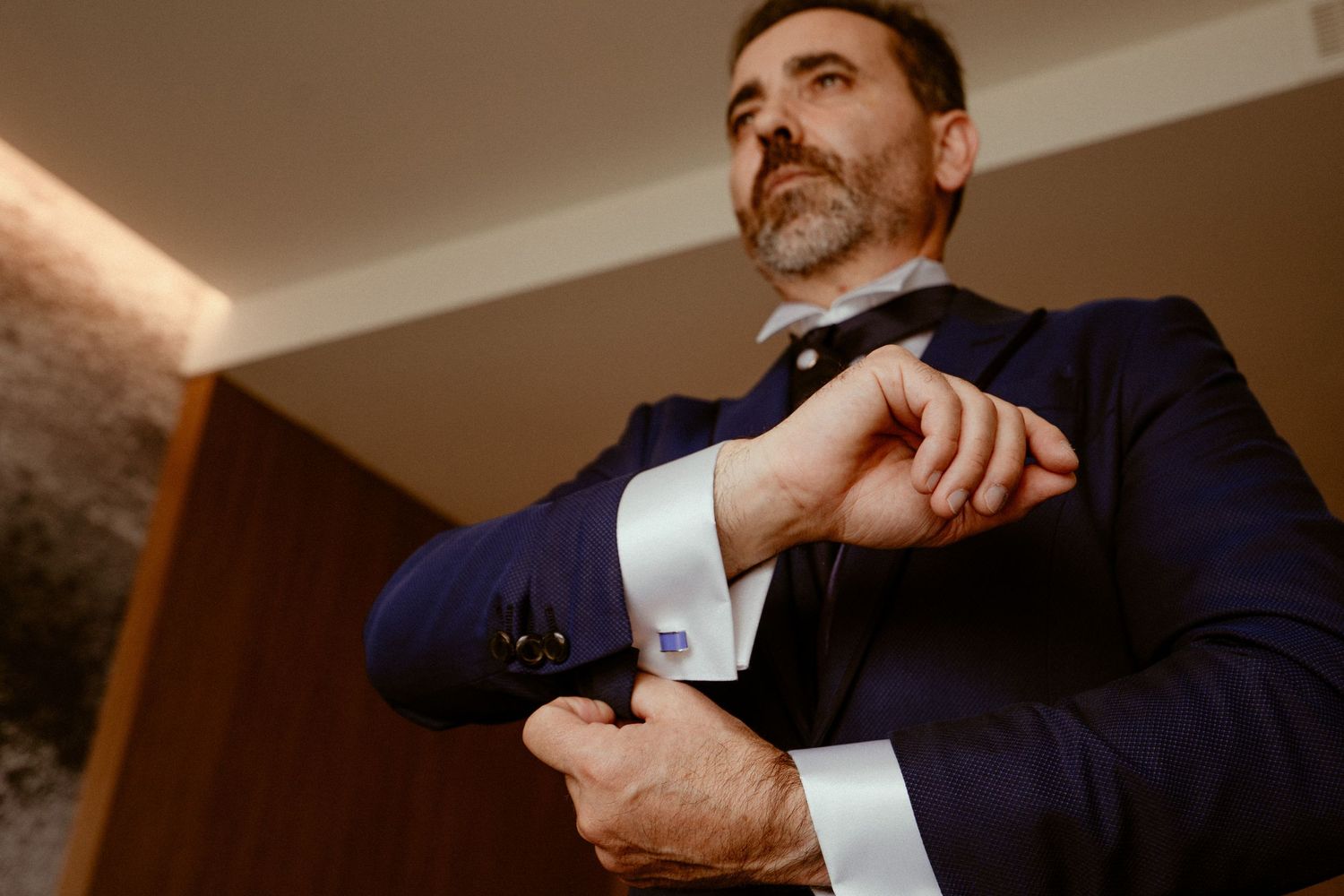 A close-up of hands adjusting formal dress shirt cuffs with cufflinks during wedding preparation.