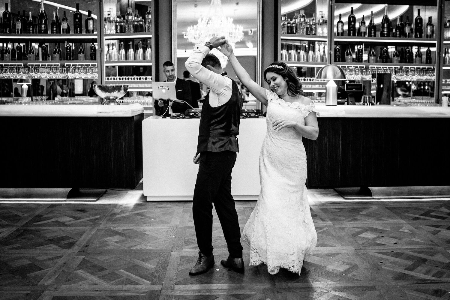 A joyful couple dancing together at a bar in black and white, with shelves of bottles visible in the background.