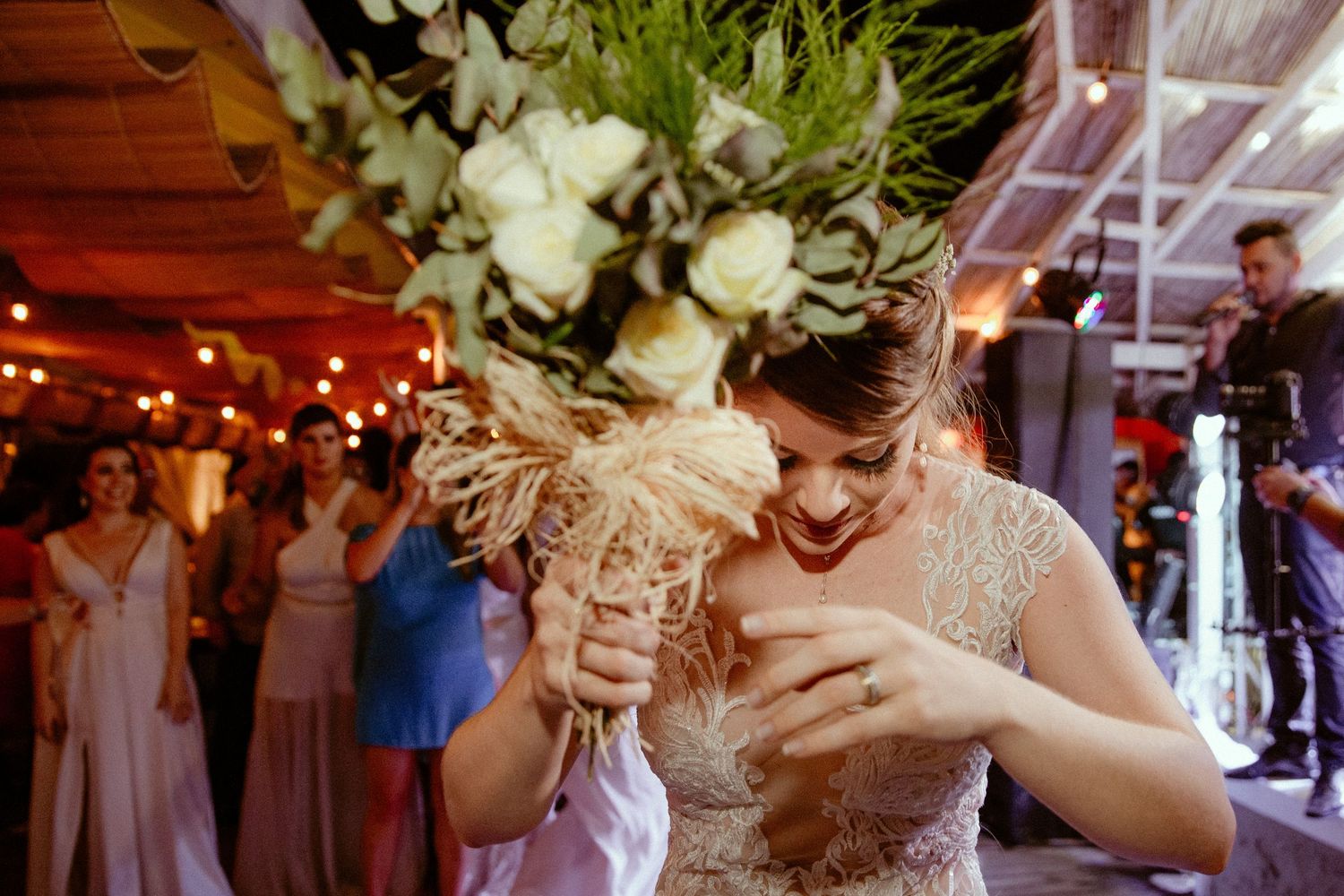 Someone in a sparkly dress catches a bouquet toss at a wedding reception with string lights and floral decorations.