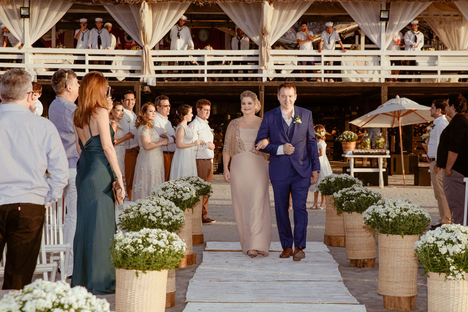 Wedding guests mingle and celebrate during an elegant outdoor reception with rustic barrels and white floral arrangements.