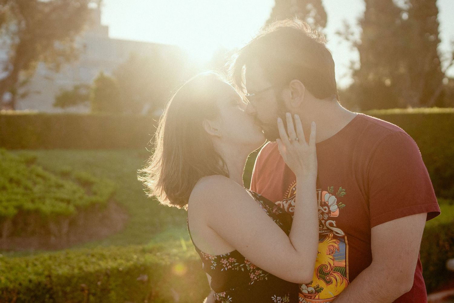 Silhouetted couple sharing romantic moment in golden sunlight flare during sunset outdoors.
