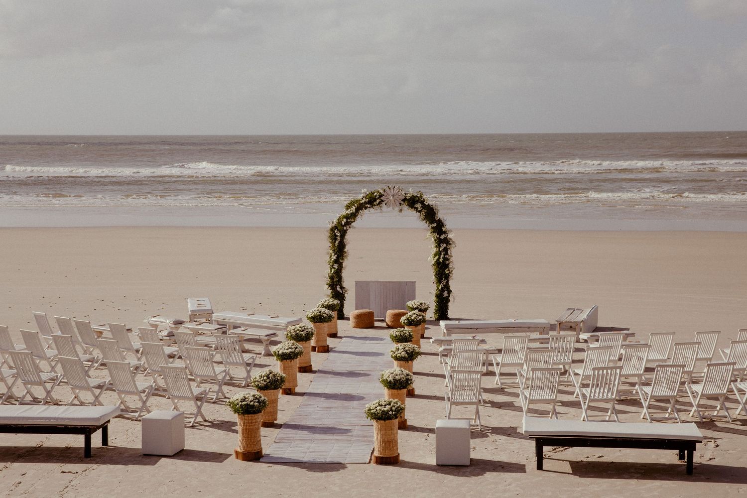 Several empty church pews with memorial markers and candles line up in front of an ocean view during an overcast day.