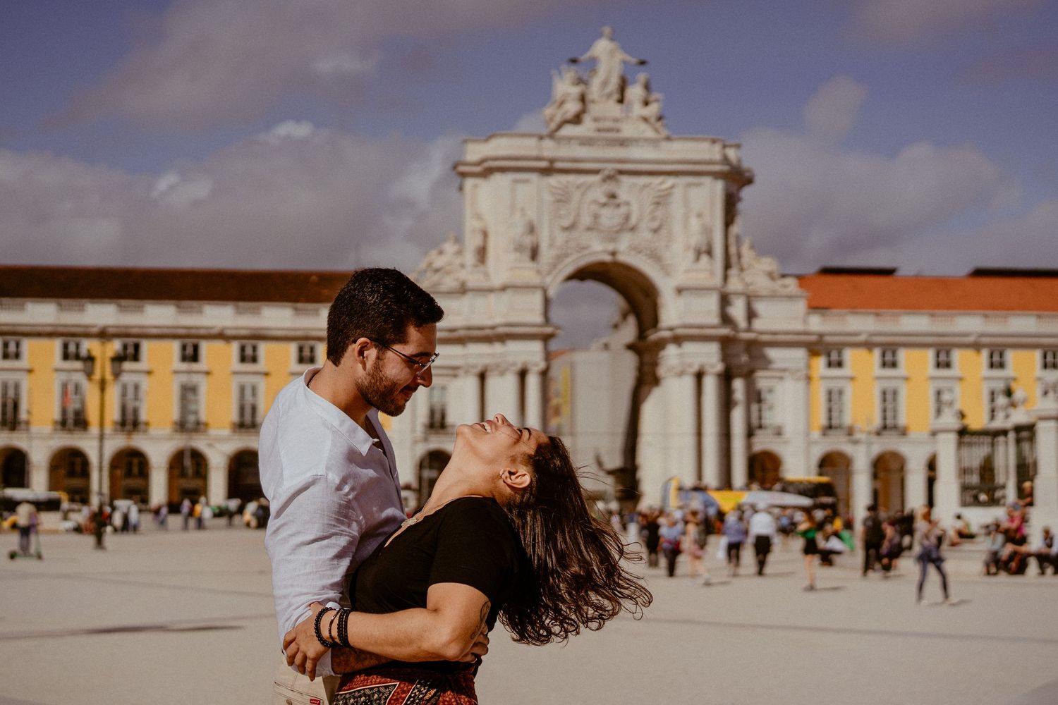 Intimate couple embraces and dances in front of ornate European architecture at a historic plaza in Lisbon, Portugal.