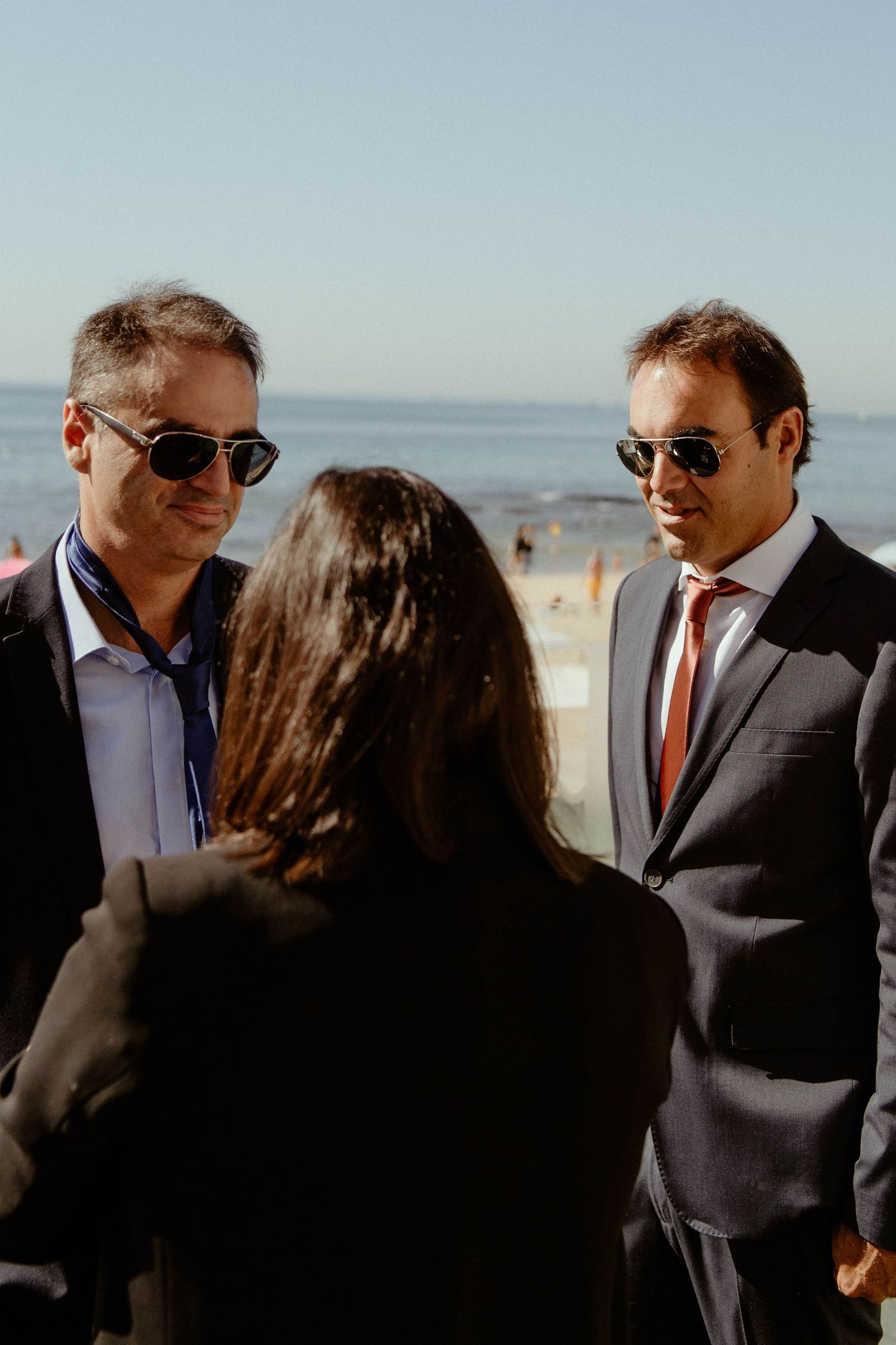 Two people in business attire having a conversation on a beach with sunlight and ocean in the background.
