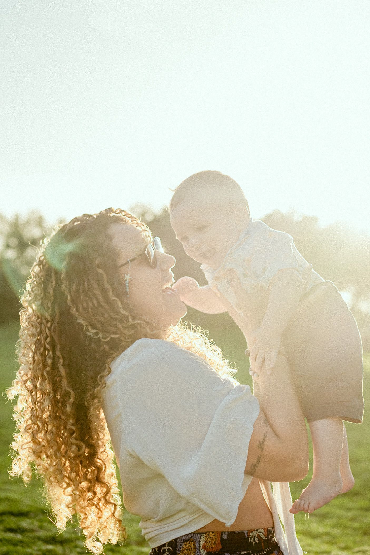 A sweet moment shared between parent and baby in golden sunlight with lens flare.