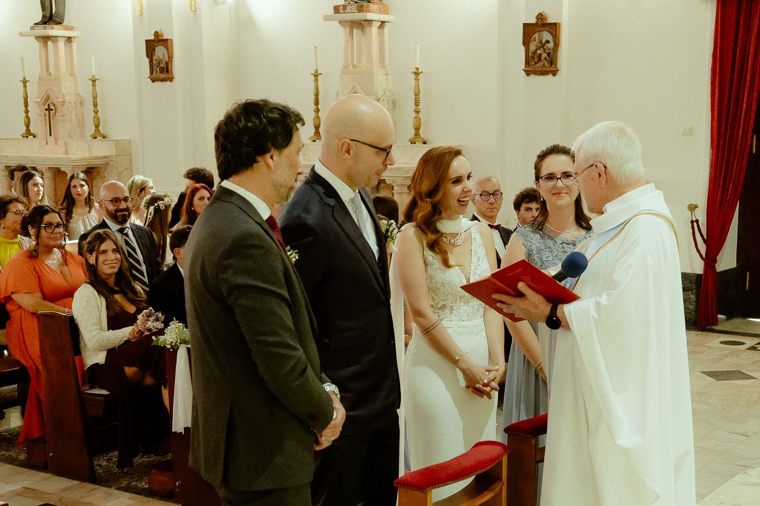 Couple exchanges wedding vows before a priest in a beautiful church ceremony with guests seated in pews.