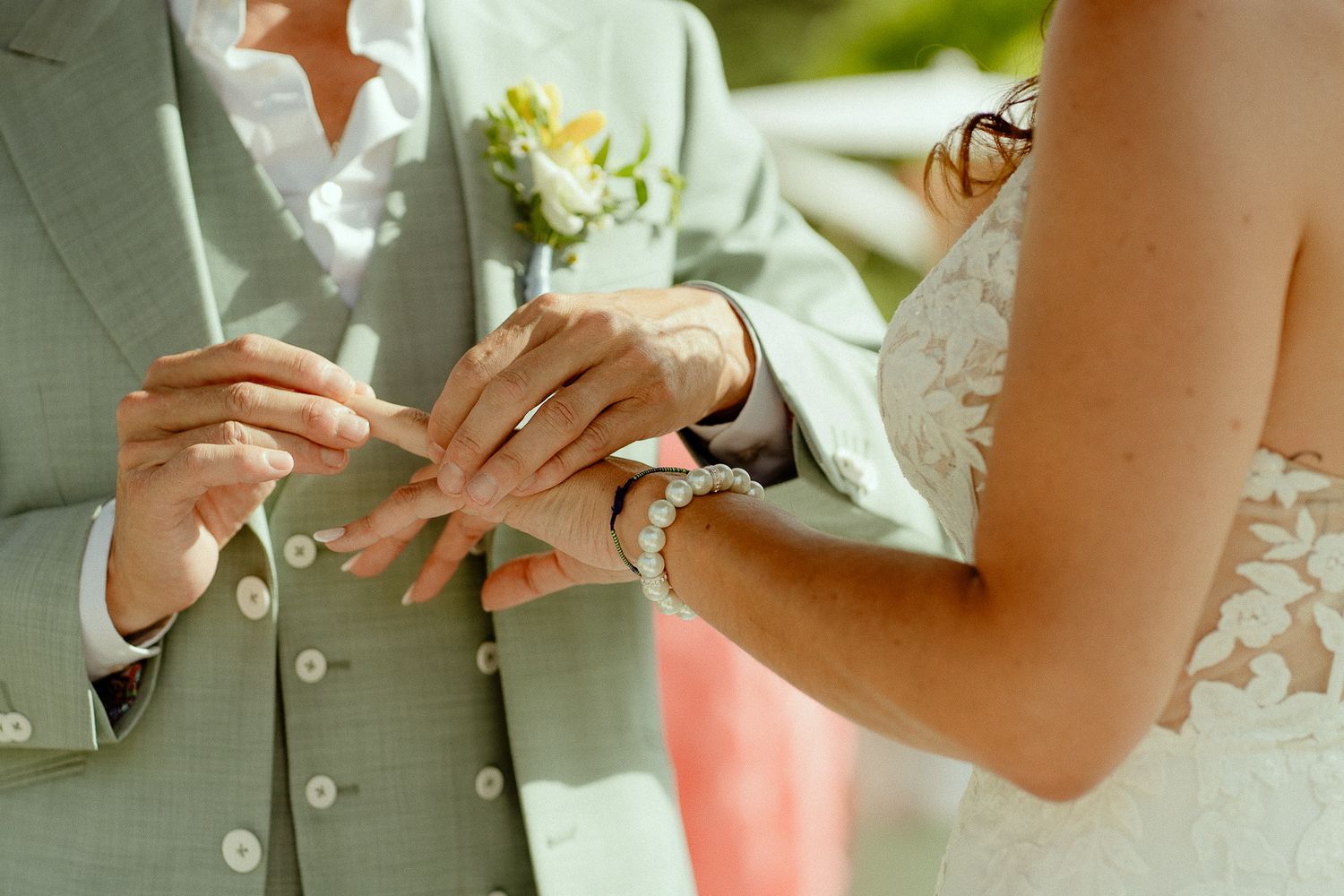 Bride placing a wedding ring on groom's finger during outdoor ceremony, groom in sage suit.