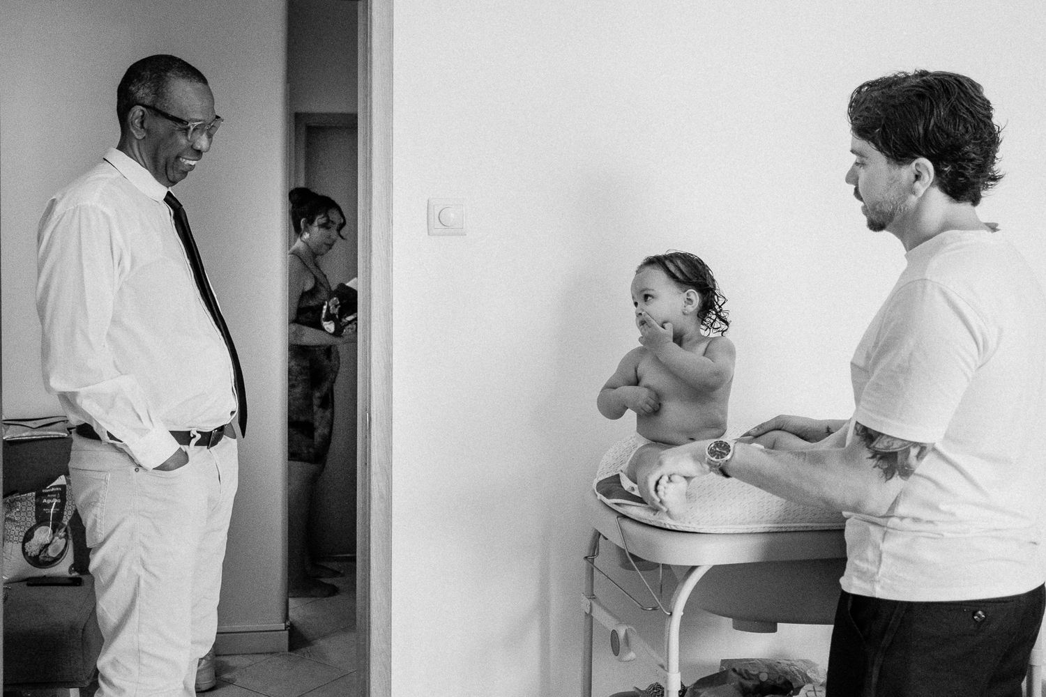 Black and white photo of a man and woman with a baby on a changing table, while another person stands in the background.