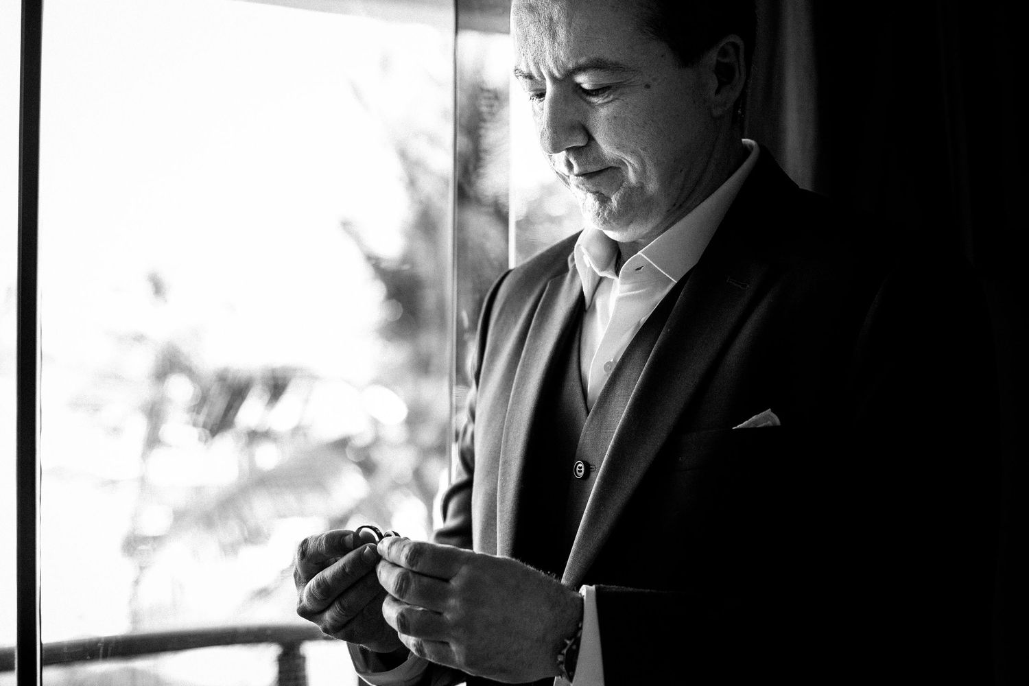 Dramatic black and white portrait of someone adjusting cufflinks by a window.