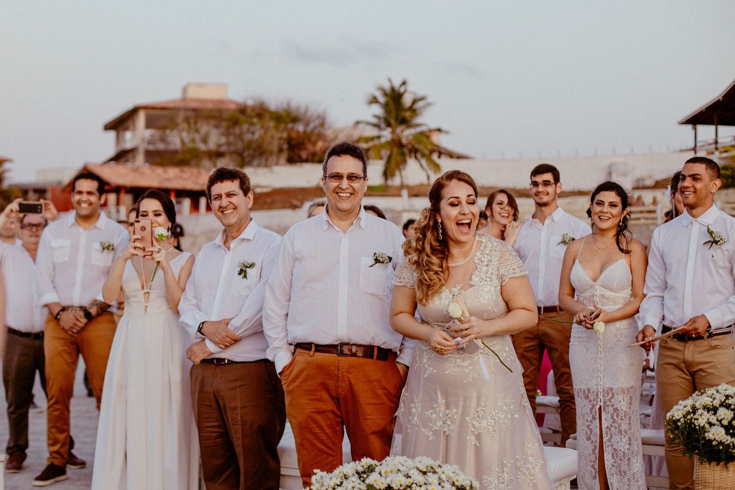 Wedding guests in white and beige attire gathered for an outdoor beach celebration.