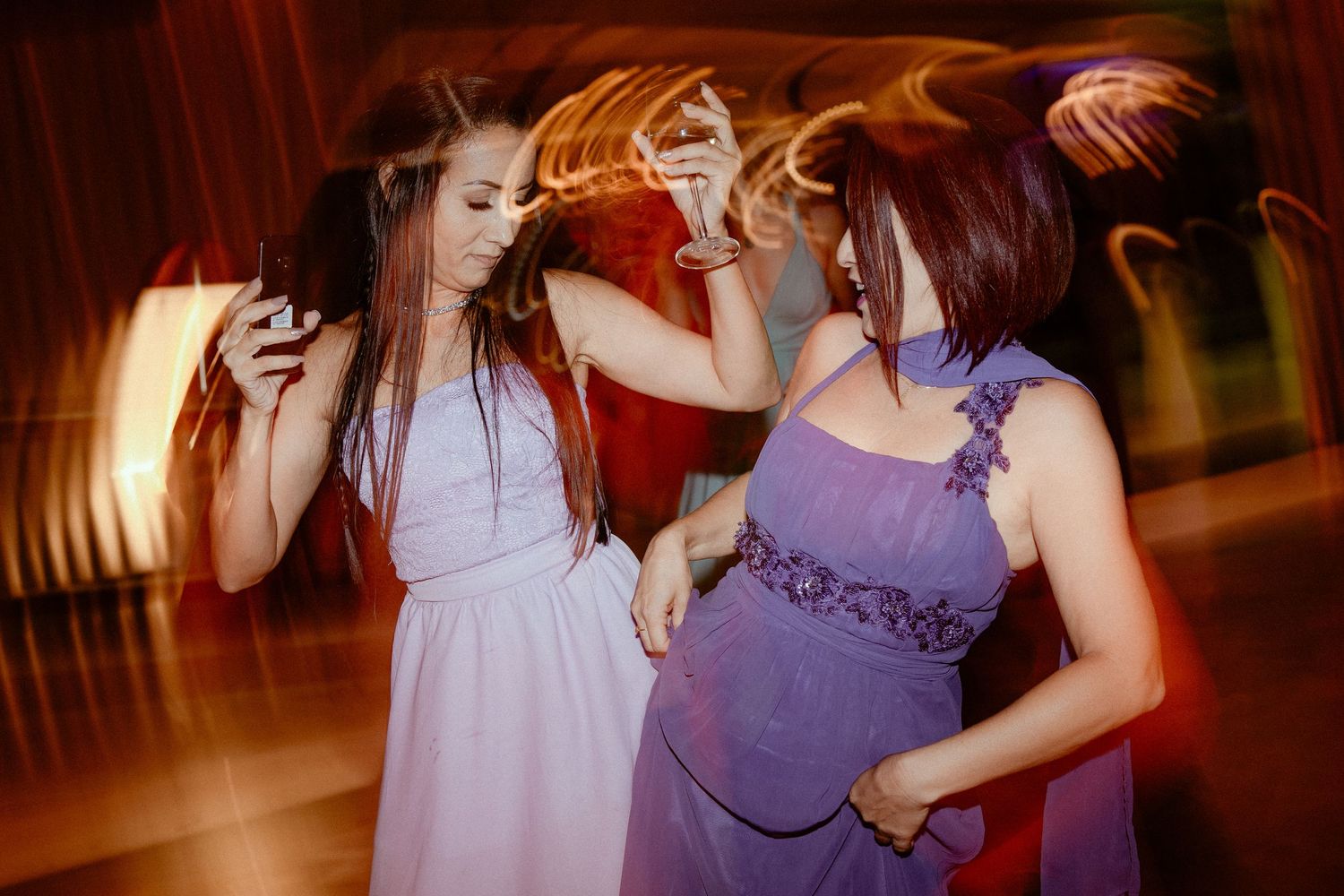 Wedding guests dance together in purple dresses and formal attire at an evening reception.