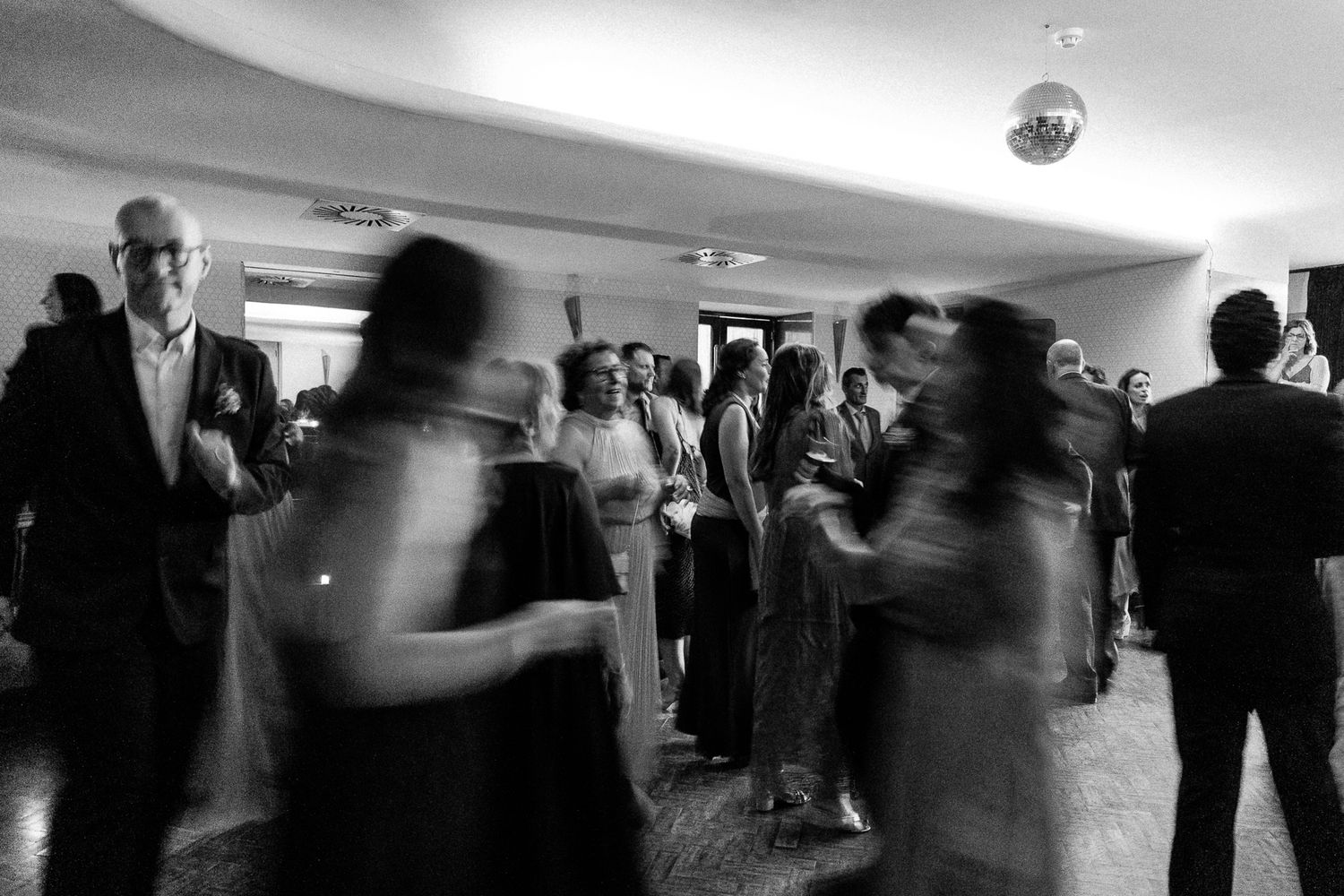Black and white photo of guests dancing at an elegant evening reception with a disco ball overhead.