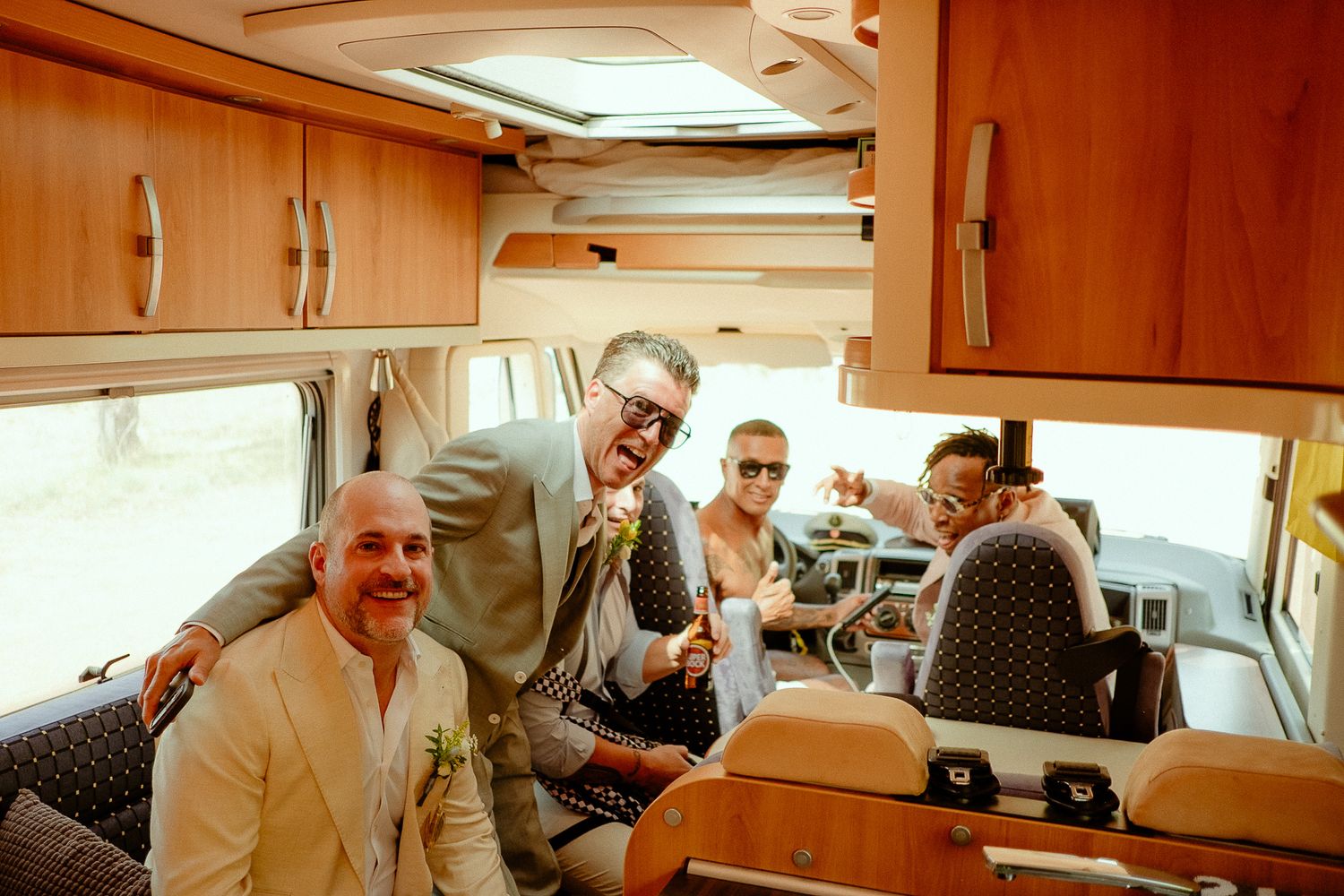 Groom in light gray suit laughing with groomsmen inside a vintage camper van.
