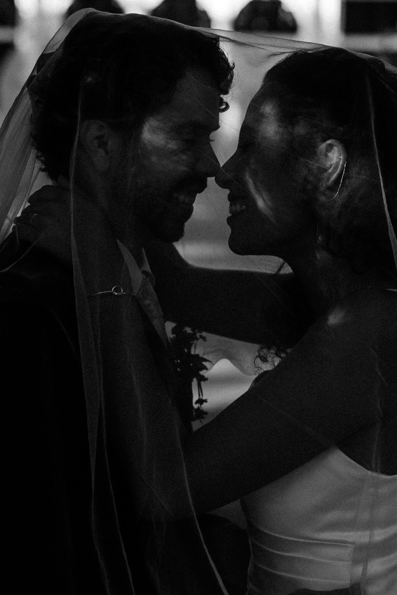 Black and white wedding photo of bride and groom sharing an intimate moment under a veil.