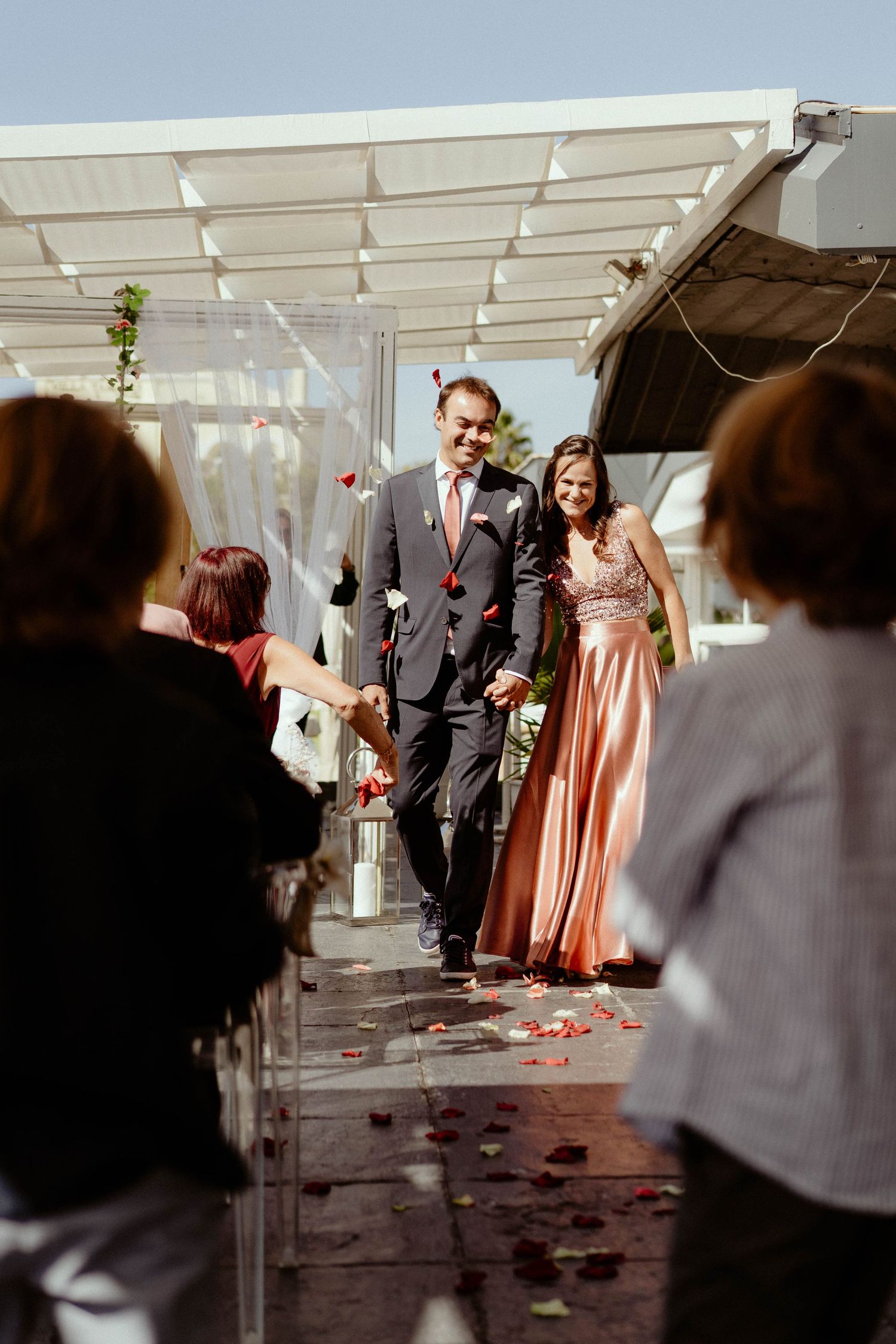 Wedding ceremony in a tent with bridesmaids in peach dresses and rose petals scattered along the aisle.