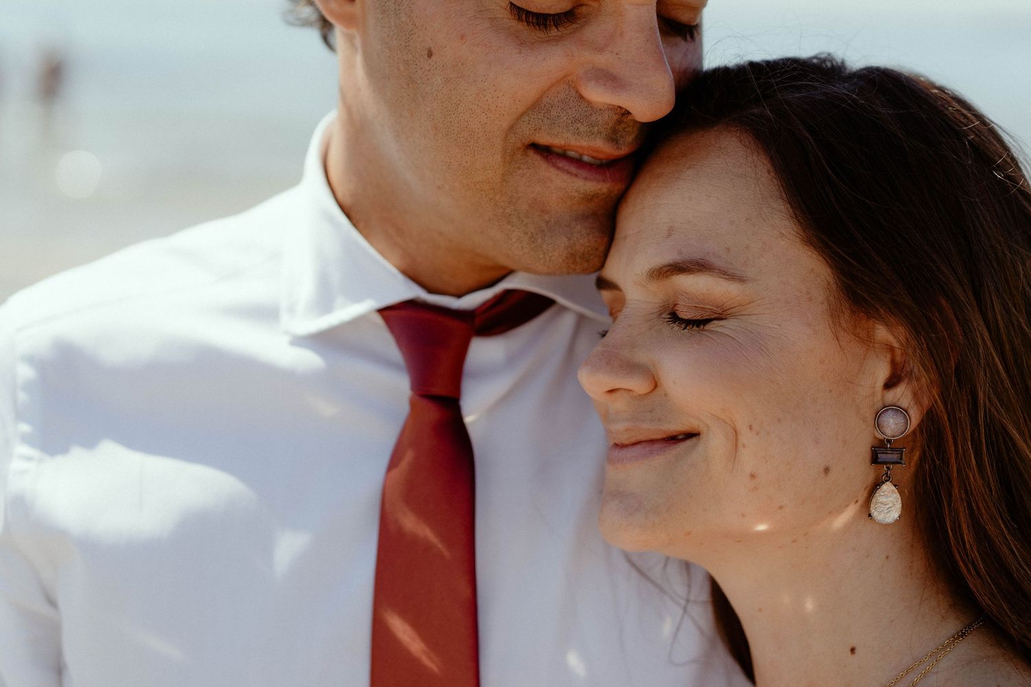 A romantic couple in formal attire share an intimate moment against a light-colored background.