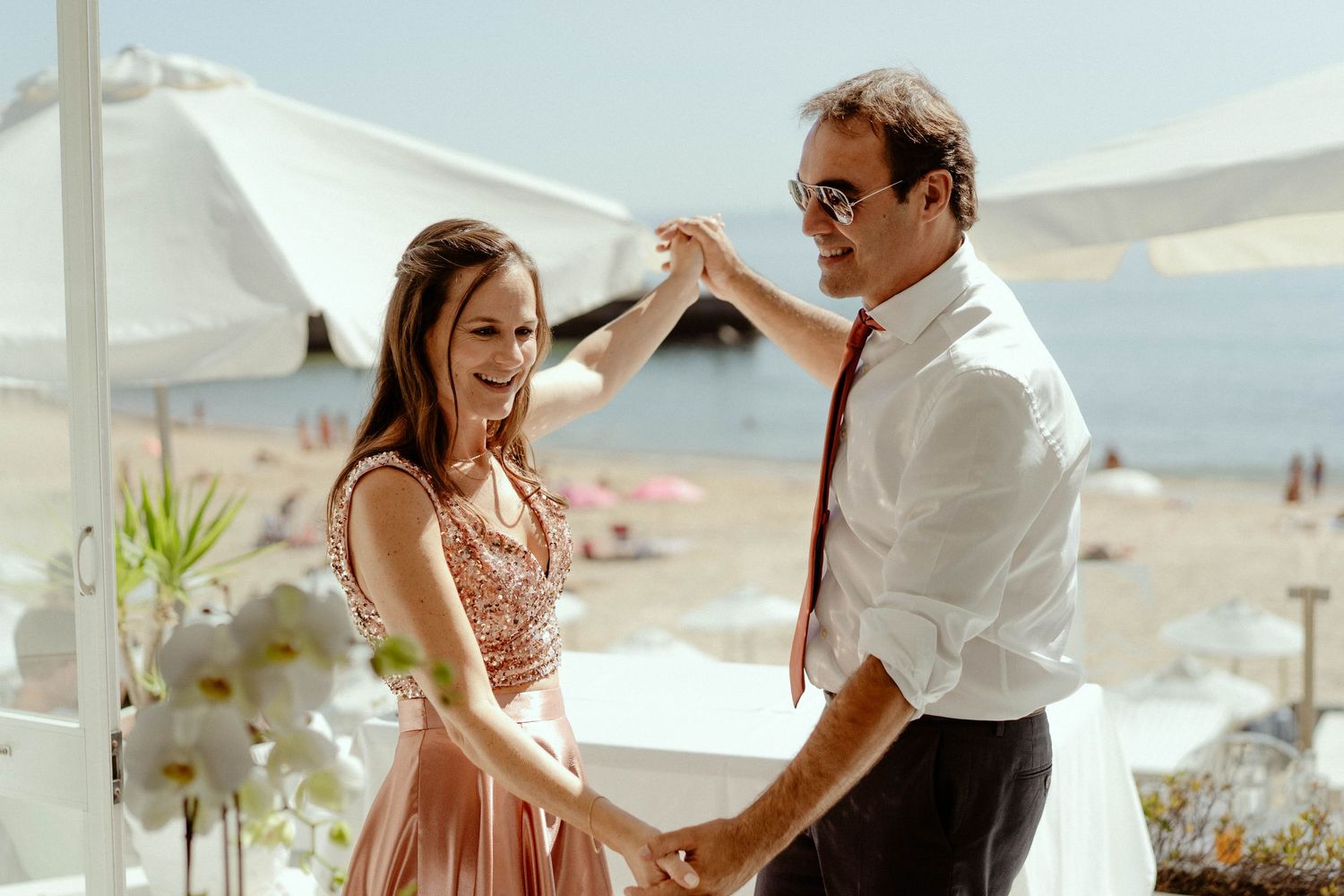 A couple dancing together at a beachside venue with white umbrellas and ocean views in the background.