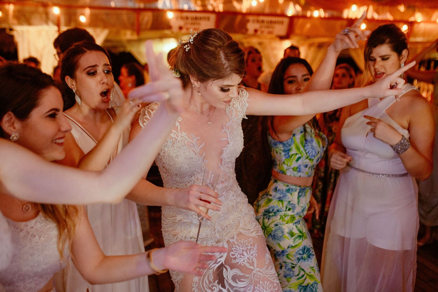 Wedding guests dance and celebrate together on a warmly lit dance floor during a reception celebration.