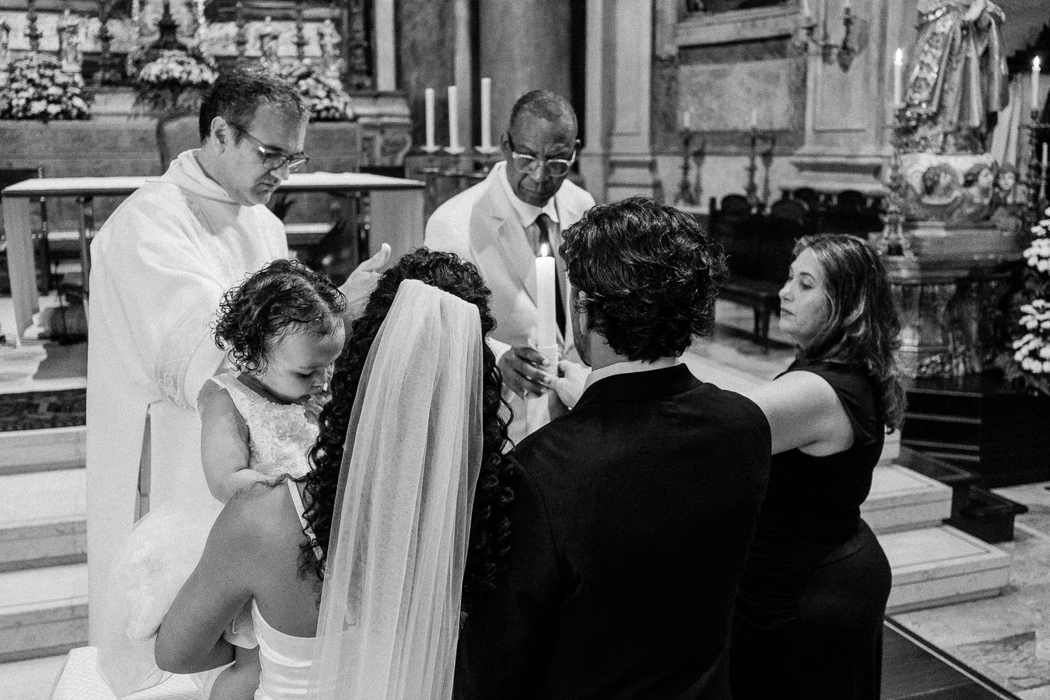 Black and white photo of a wedding ceremony in a church with priest, bride, groom, and guests gathered at the altar.