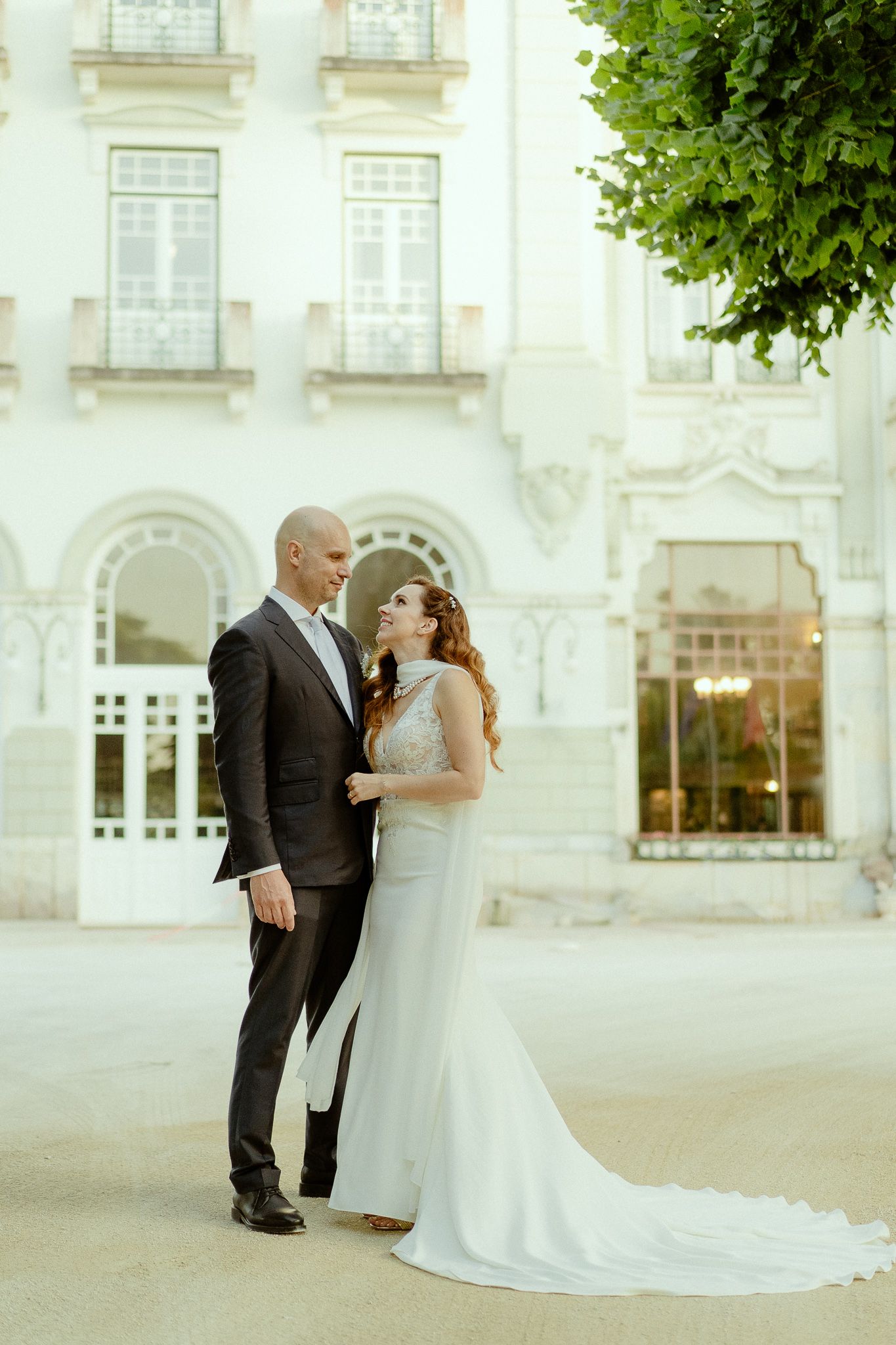 Elegant bride and groom embracing in front of a grand white European building on their wedding day.